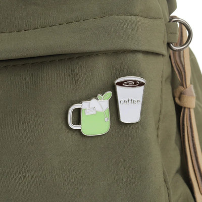 Two pins on a green backpack: one resembling a green drink with a straw and the other a coffee cup.