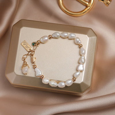 Pearl bracelet with gold accents on a decorative box against a beige fabric background
