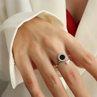 Hand wearing a steel color ring with a black gemstone on a neutral background