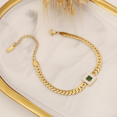 Gold bracelet with a green gemstone on a beige surface