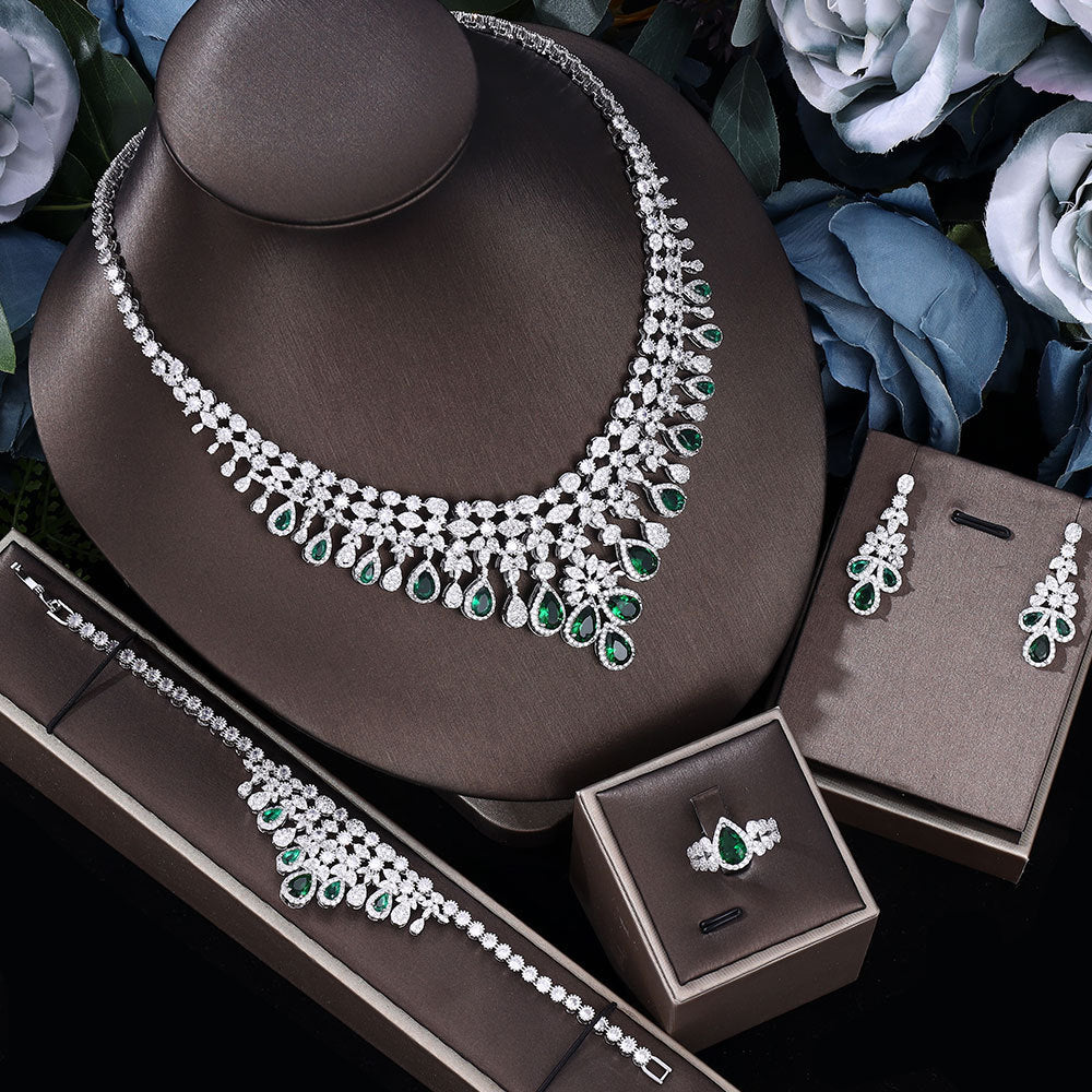 green zircon bridal Jewelry set including necklace, earrings, ring  and bracelet on a brown stand with flowers in the background.