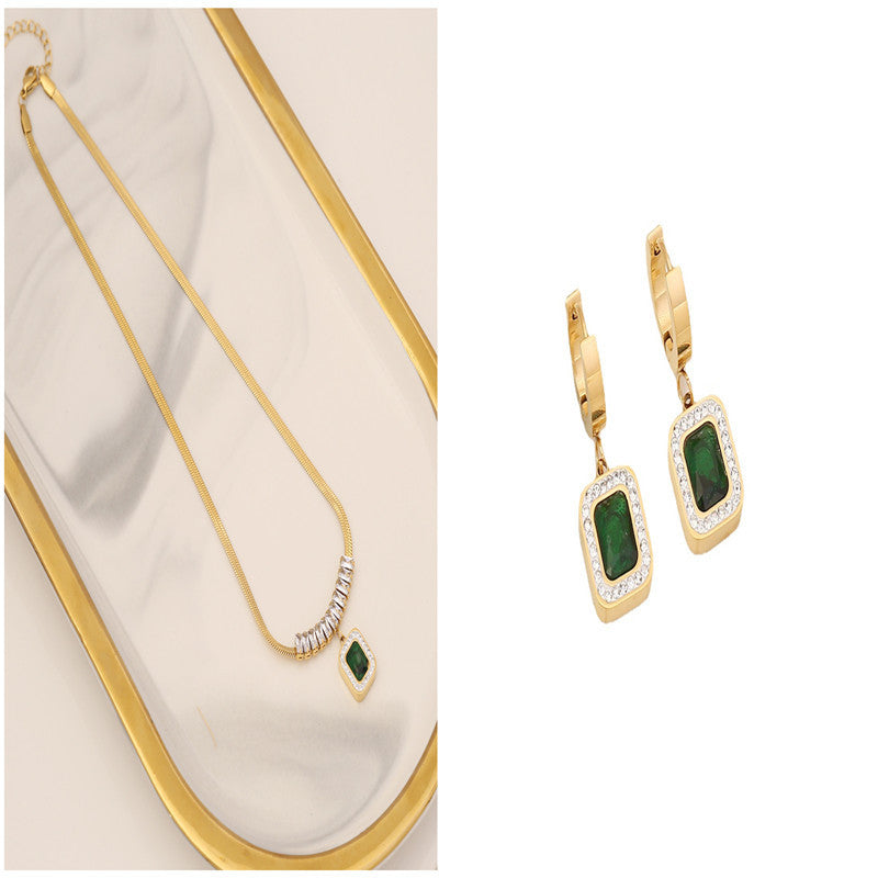 Gold necklace and earrings with green gemstones on a white background