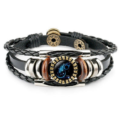 A stylish black leather bracelet with braided strands features a circular zodiac-themed charm in the center, surrounded by metallic and wooden accents.