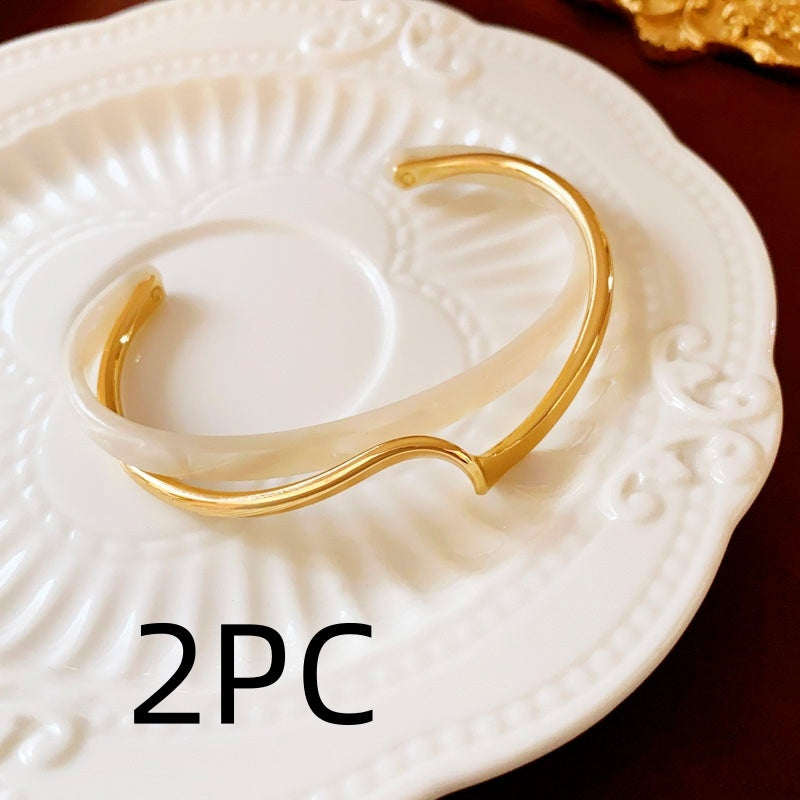 Gold bracelet on a white decorative plate with '2PC' text.