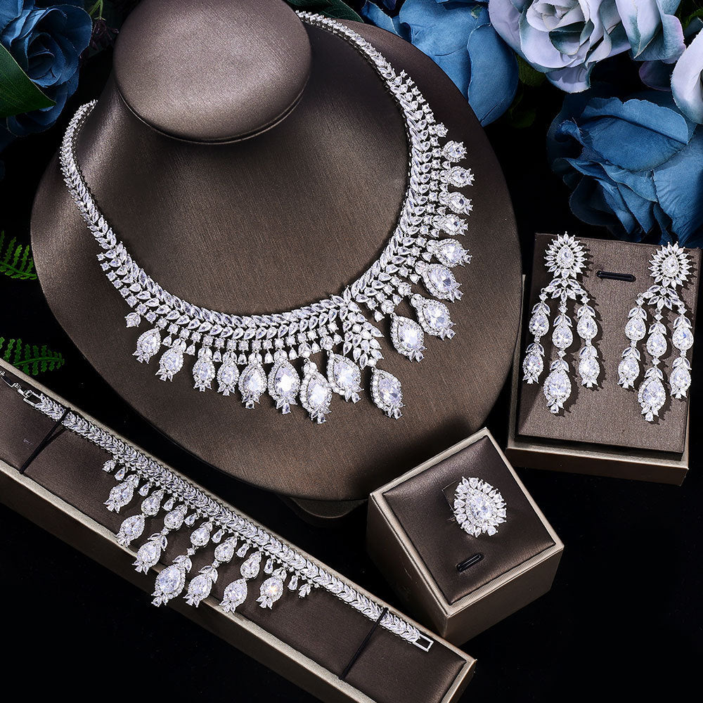 Bridal zircon jewelry set, necklace, bracelet, ring and earrings on a dark surface with flowers in the background