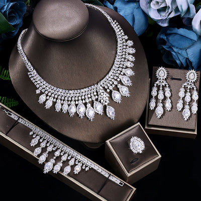 Bridal zircon jewelry set, necklace, bracelet, ring and earrings on a dark surface with flowers in the background