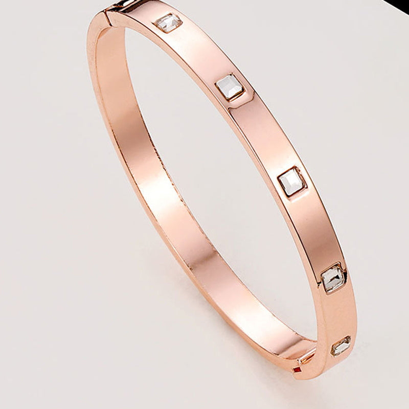 Rose gold bracelet with embedded stones on a light gray background