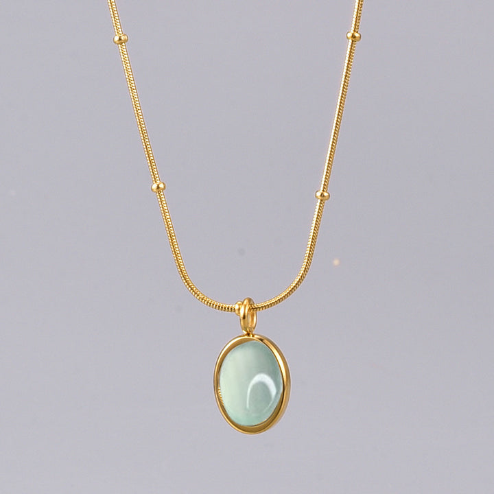 Gold necklace with a light green pendant on a gray background