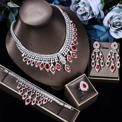 Red stone Bridal Jewelry set with necklace, earrings, and ring on a dark surface with flowers in the background