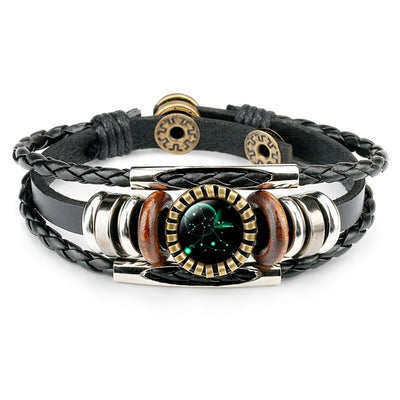 A stylish black braided and leather bracelet featuring a circular zodiac constellation center, metal accents, and wooden beads. It conveys a trendy, celestial vibe.