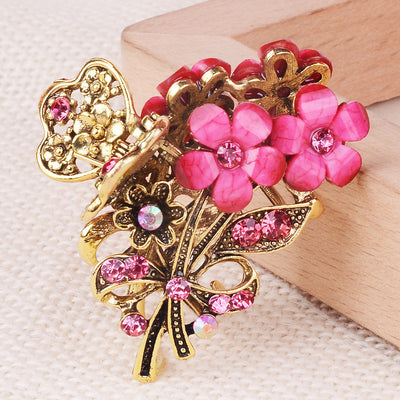 Decorative hair clip with pink flowers and gold butterfly on a textured surface