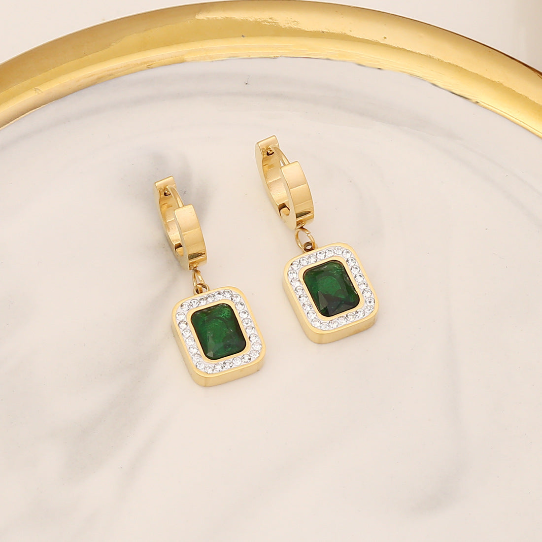 Gold hoop earrings with green gemstones on a beige background