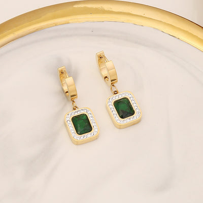 Gold hoop earrings with green gemstones on a beige background