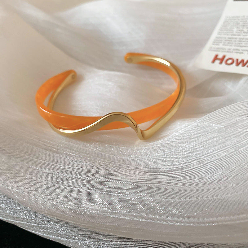 Gold bracelet with orange band on a white fabric background