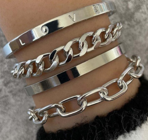 four silver bracelets stacked on a wrist against a neutral background
