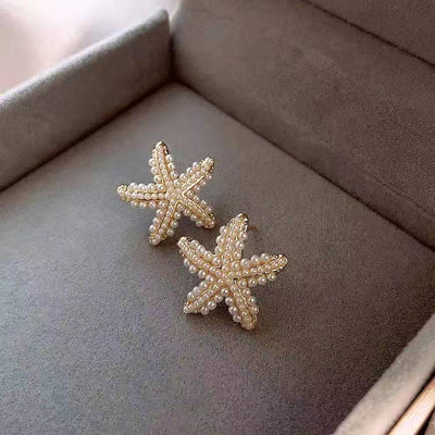 Starfish-shaped earrings with pearls on a gray surface