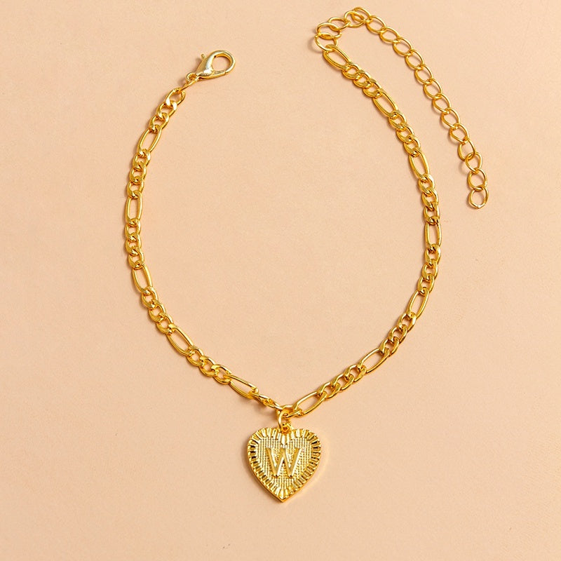 Gold chain bracelet with a heart-shaped charm letter W on a beige background