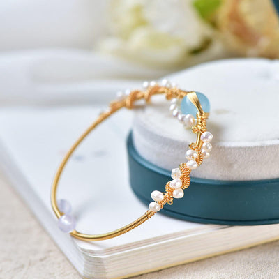 Gold bracelet with pearls and blue stone on a white surface