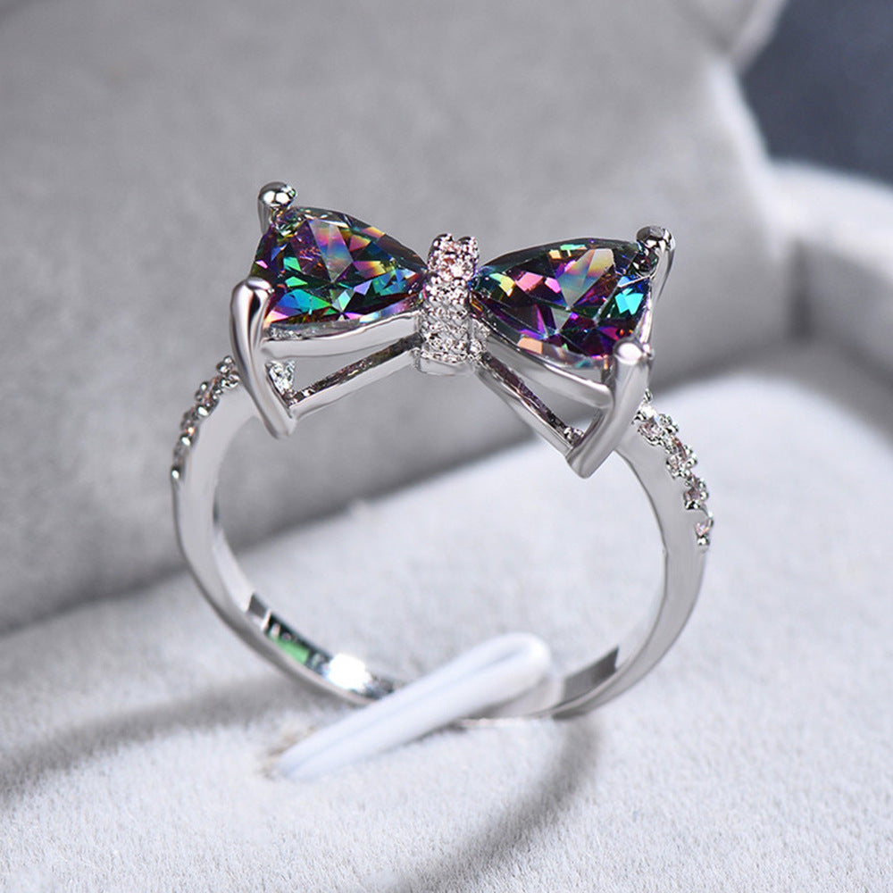 Silver bow-shaped ring with colorful gemstones on a soft fabric background