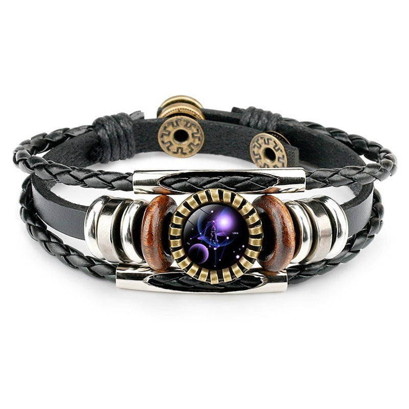 A stylish black leather bracelet with braided and smooth strands features metallic and wooden beads, centering a round zodiac-themed pendant.