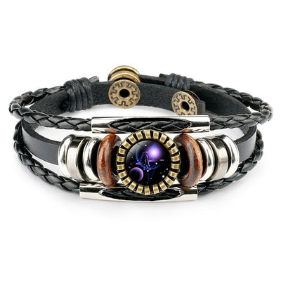 A stylish black leather bracelet with braided and smooth strands features metallic and wooden beads, centering a round zodiac-themed pendant.
