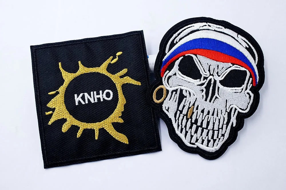 Two patches on a white background, one with a sun and 'KNHO' text, the other with a skull design.