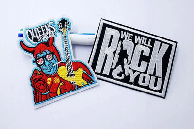 Two patches on a white background, one with a devil playing guitar and 'Queens' text, the other with 'We Will Rock You' text.
