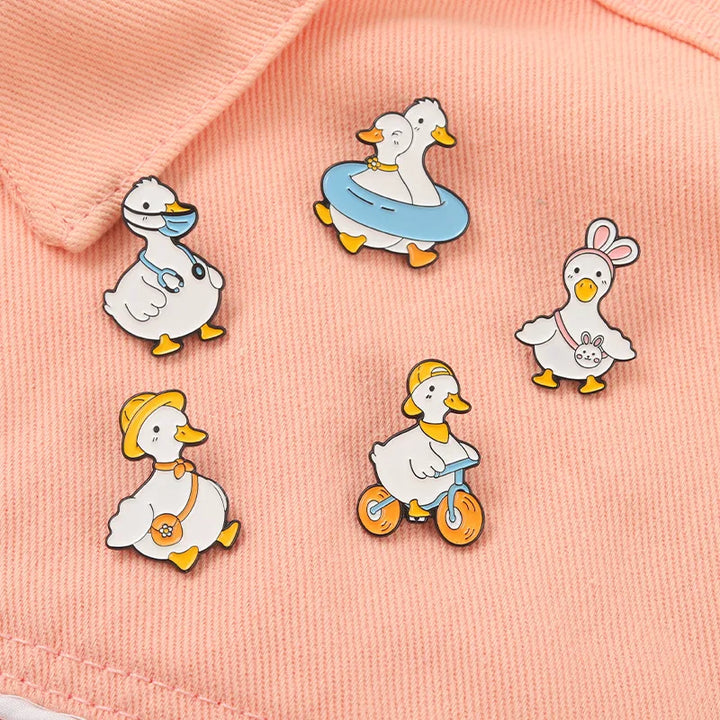 Set of cartoon duck pins on a pink fabric background