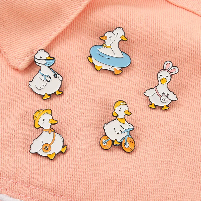 Set of cartoon duck pins on a pink fabric background