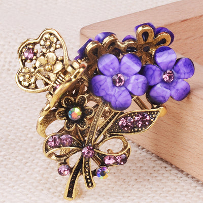 Decorative hair clip with purple flowers and gold butterfly design on a wooden surface.