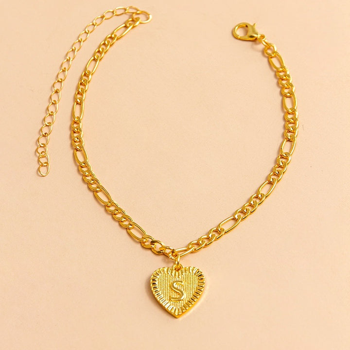 Gold chain bracelet with a heart-shaped pendant letter S on a beige background