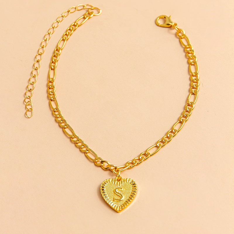 Gold chain bracelet with a heart-shaped pendant letter S on a beige background