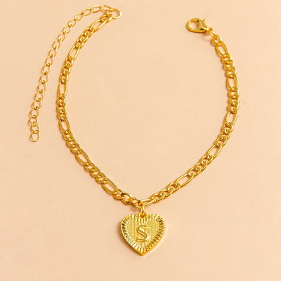 Gold chain bracelet with a heart-shaped pendant letter S on a beige background
