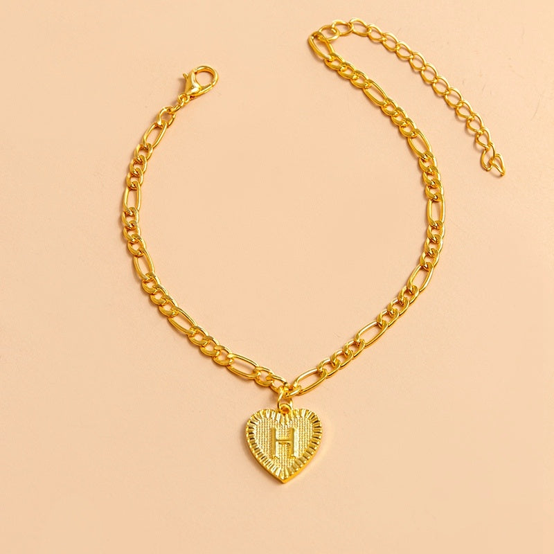 Gold chain bracelet with a heart-shaped pendant letter H on a beige background