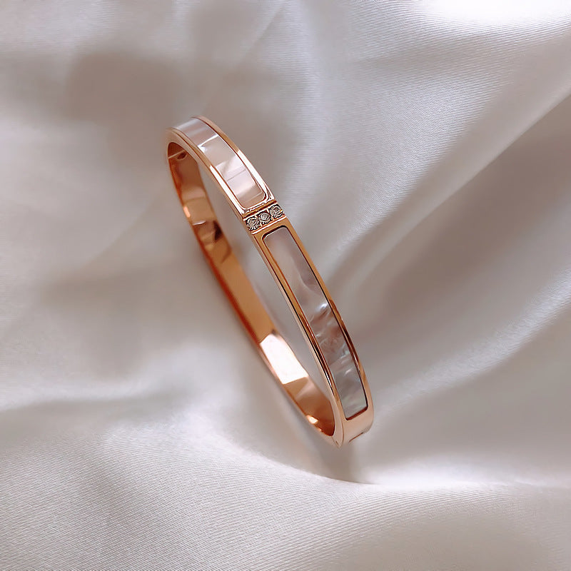 Rose gold bracelet with a white stone on a soft beige fabric background