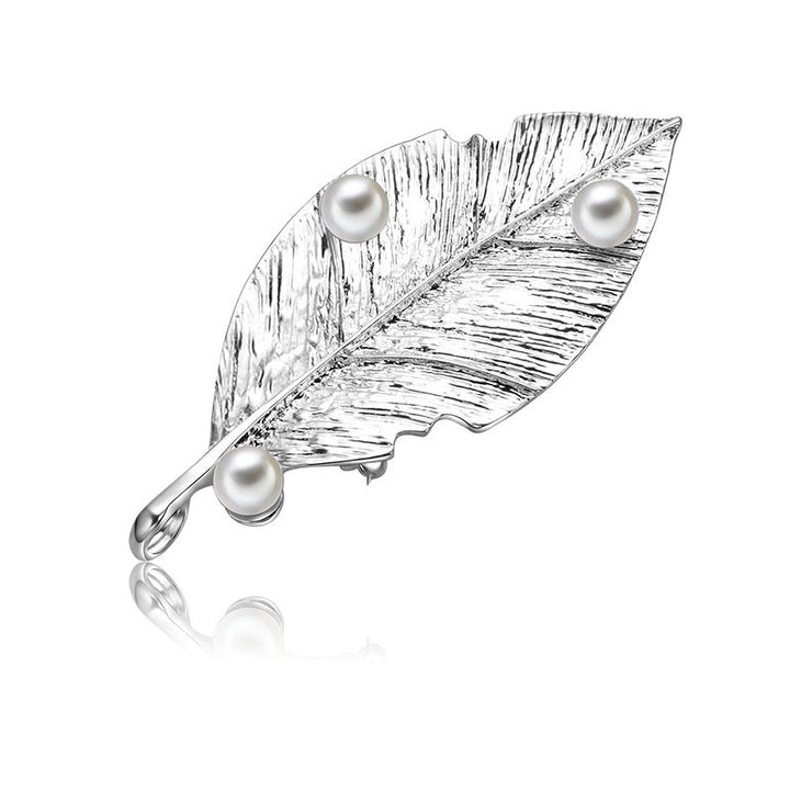 Silver leaf-shaped brooch with three pearls on a white background