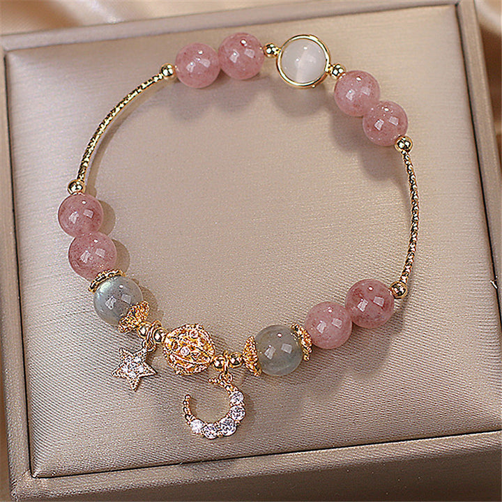Bracelet with pink and green beads and gold charms on a beige jewelry box