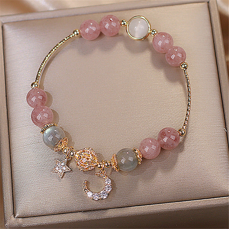 Bracelet with pink and green beads and gold charms on a beige jewelry box