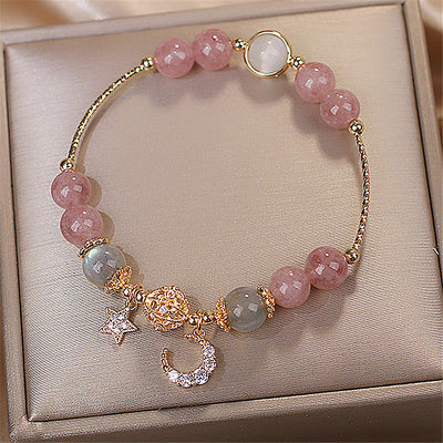 Bracelet with pink and green beads and gold charms on a beige jewelry box