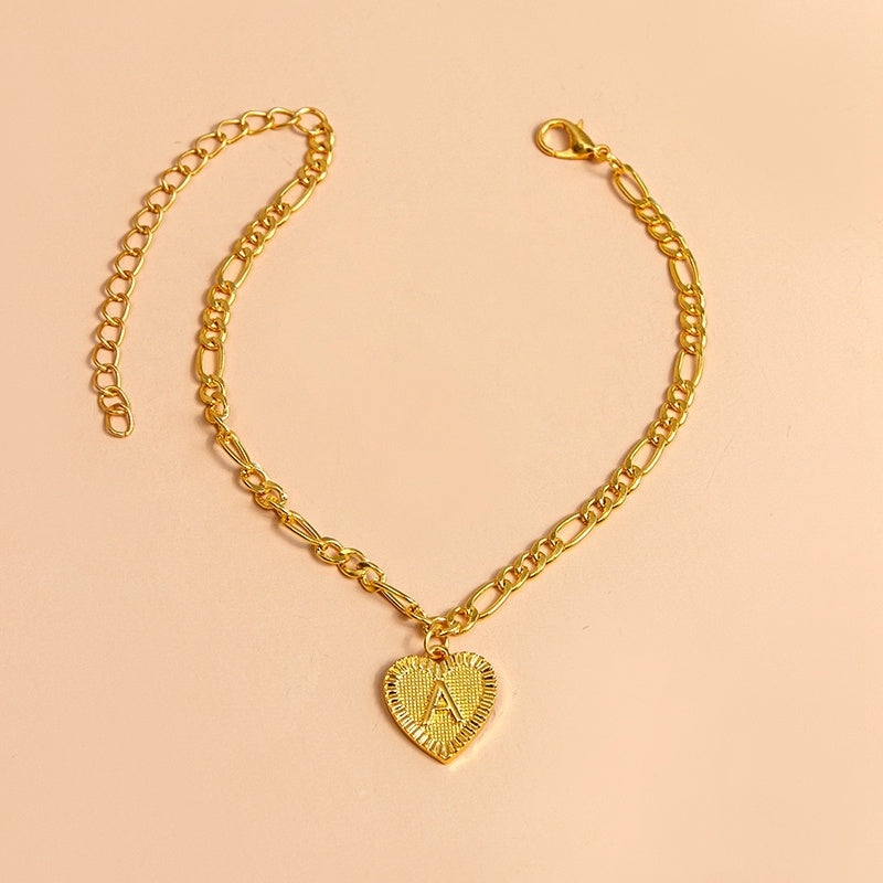 Gold chain bracelet with a heart-shaped pendant letter A on a beige background