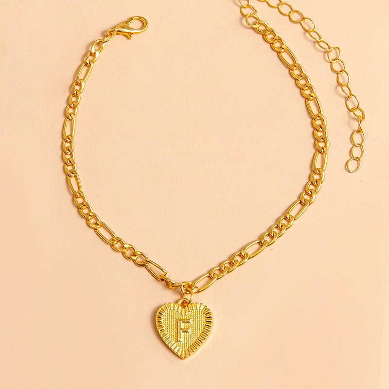 Gold chain necklace with a heart-shaped pendant letter F on a beige background
