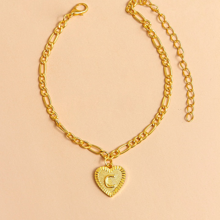 Gold chain anklet with a heart-shaped pendant letter C on a beige background