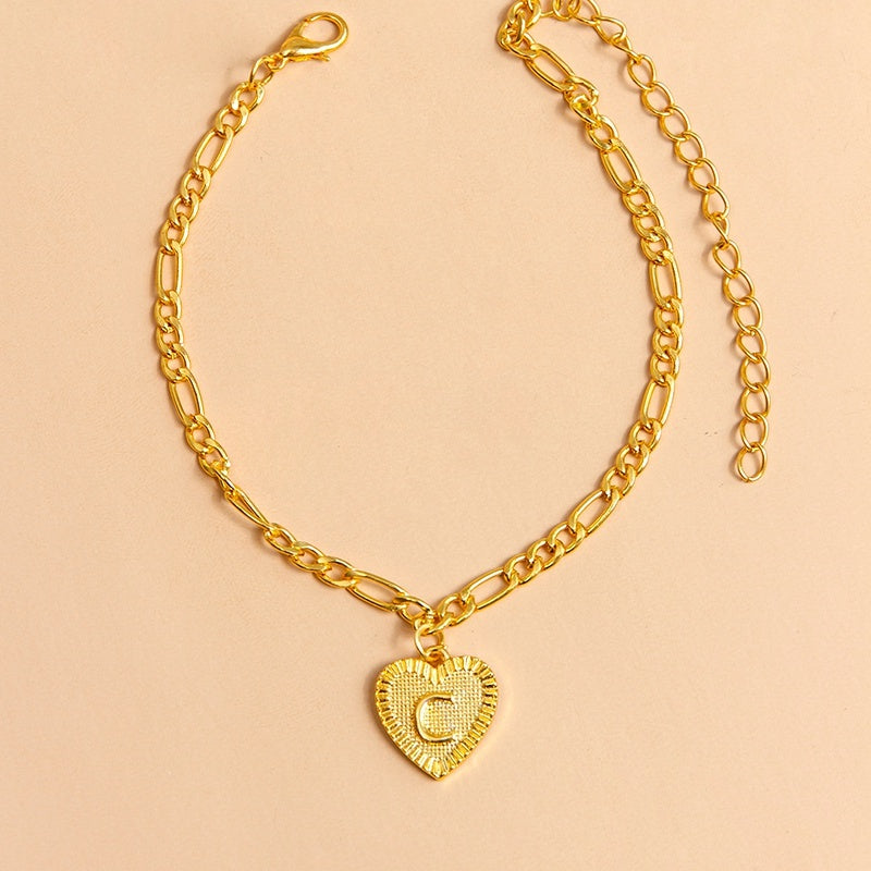 Gold chain anklet with a heart-shaped pendant letter C on a beige background