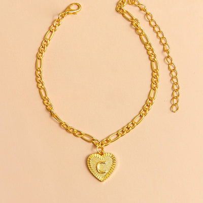 Gold chain anklet with a heart-shaped pendant letter C on a beige background