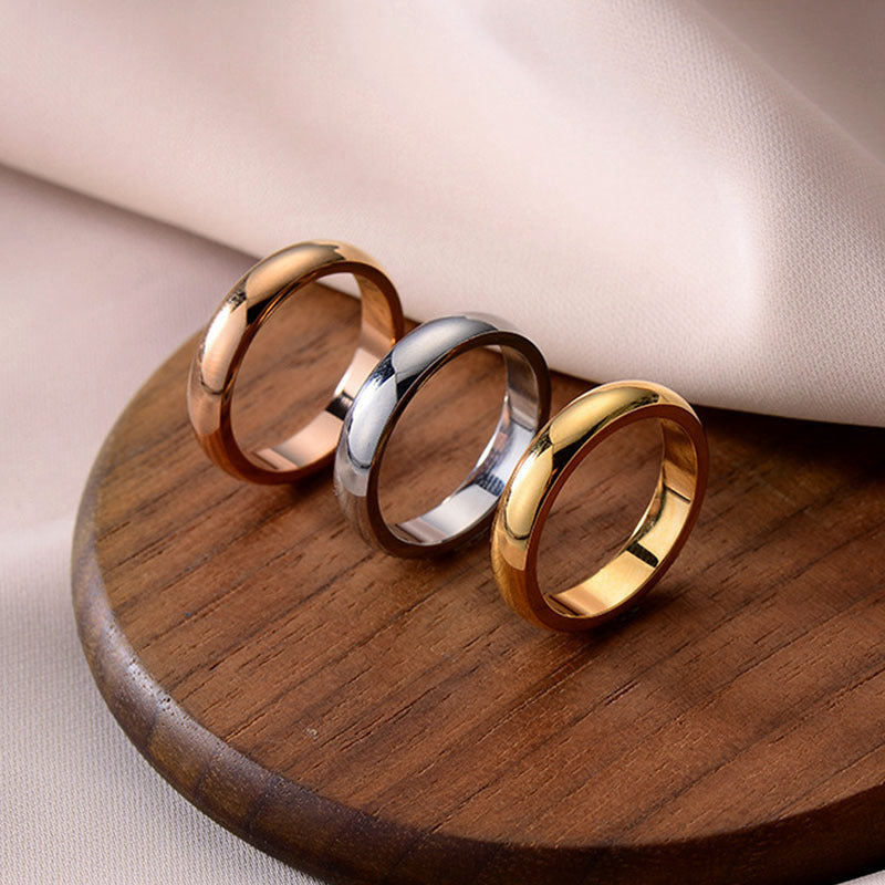 Three rings in gold, rose gold, and silver on a wooden surface with a soft beige background.