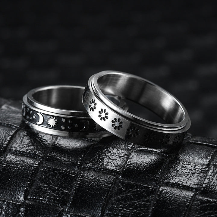 Two silver rings with intricate designs on a textured black surface