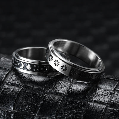 Two silver rings with intricate designs on a textured black surface