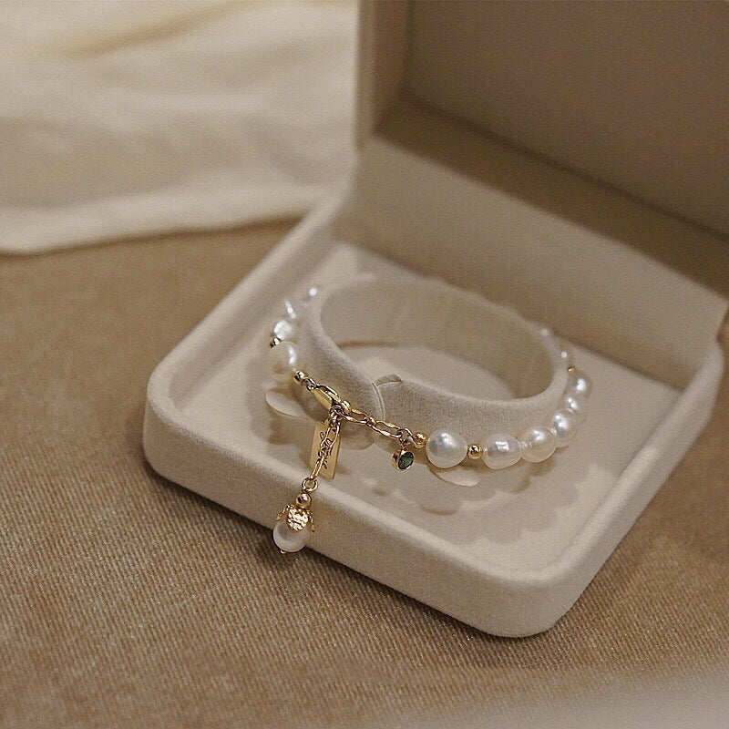 Pearl bracelet with gold charm in a jewelry box on a beige fabric background