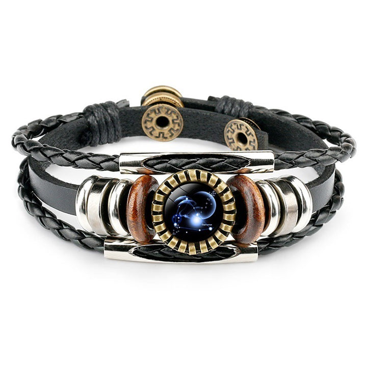 A black leather bracelet with braided and smooth bands. Features a metallic centerpiece with a celestial design, flanked by wooden and metallic accents. Elegant and modern.