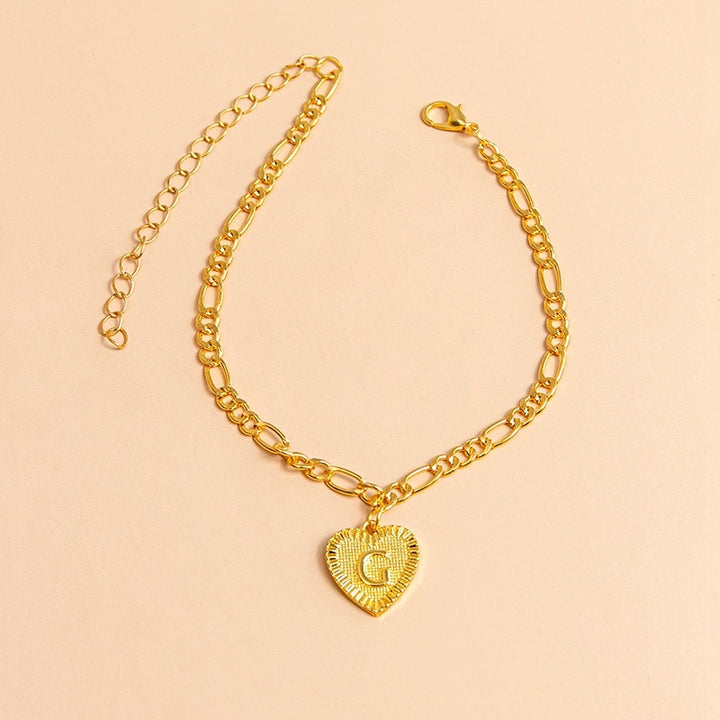 Gold bracelet with a heart-shaped charm letter G on a beige background